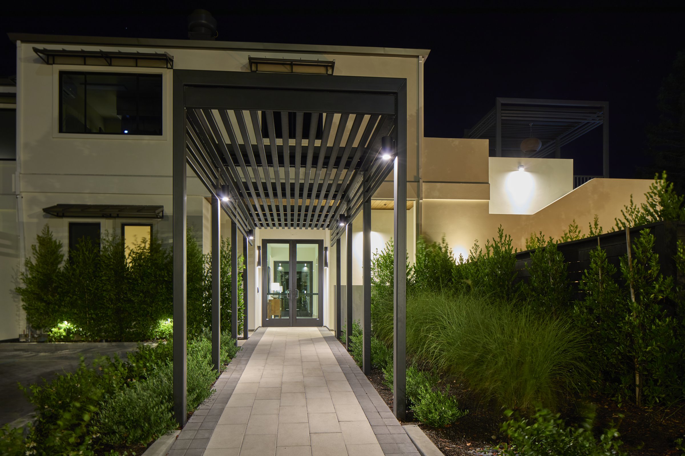 The front entry pergola and lit stone walkway at night.