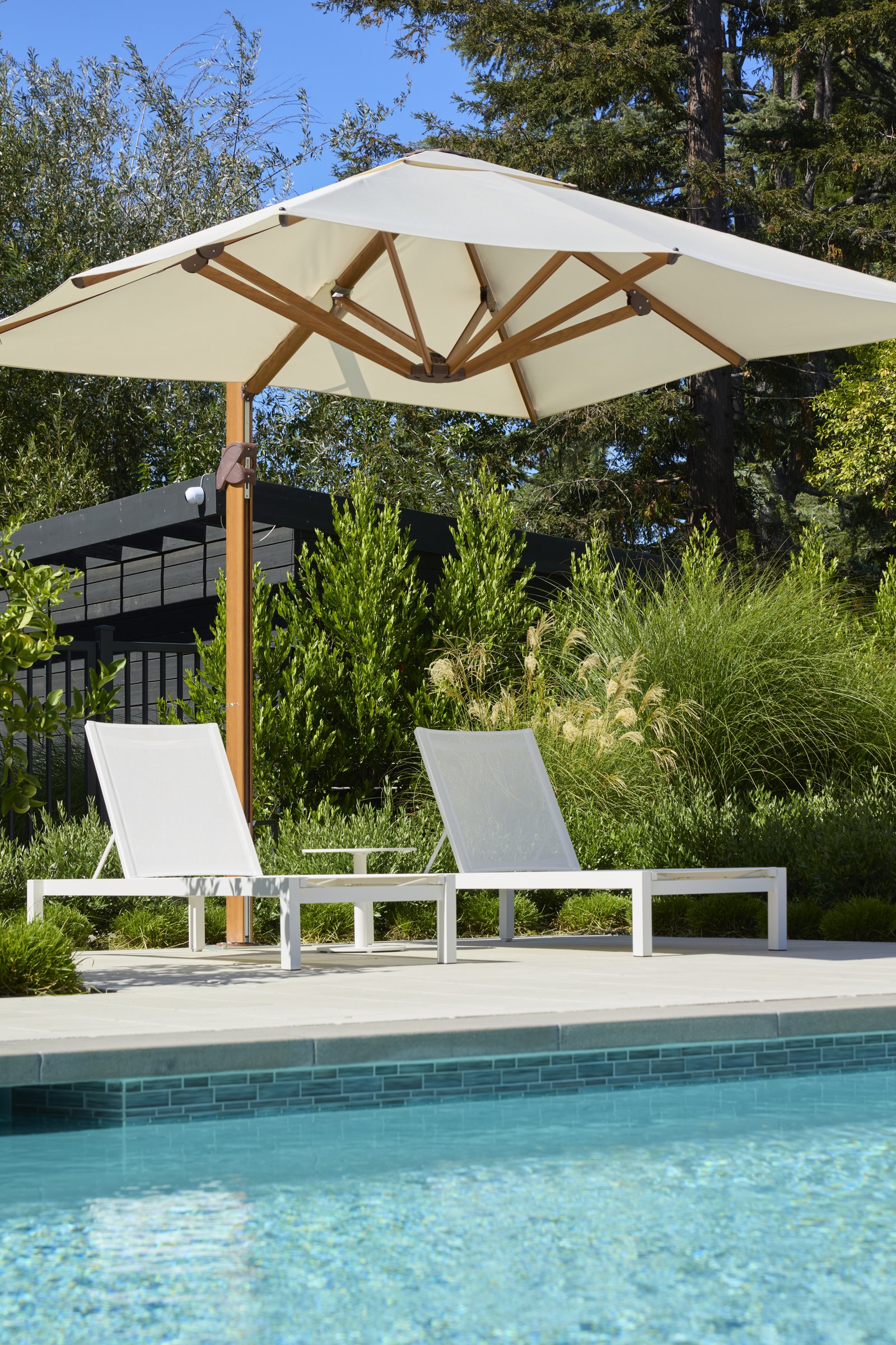 Two chaise lounges under a cantilevered umbrella at the pool's edge.
