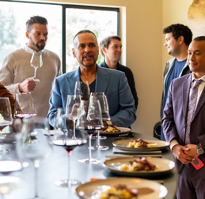 Guests in jackets and suits gathered around a long table of plated courses and poured red wine at a private corporate dinner.