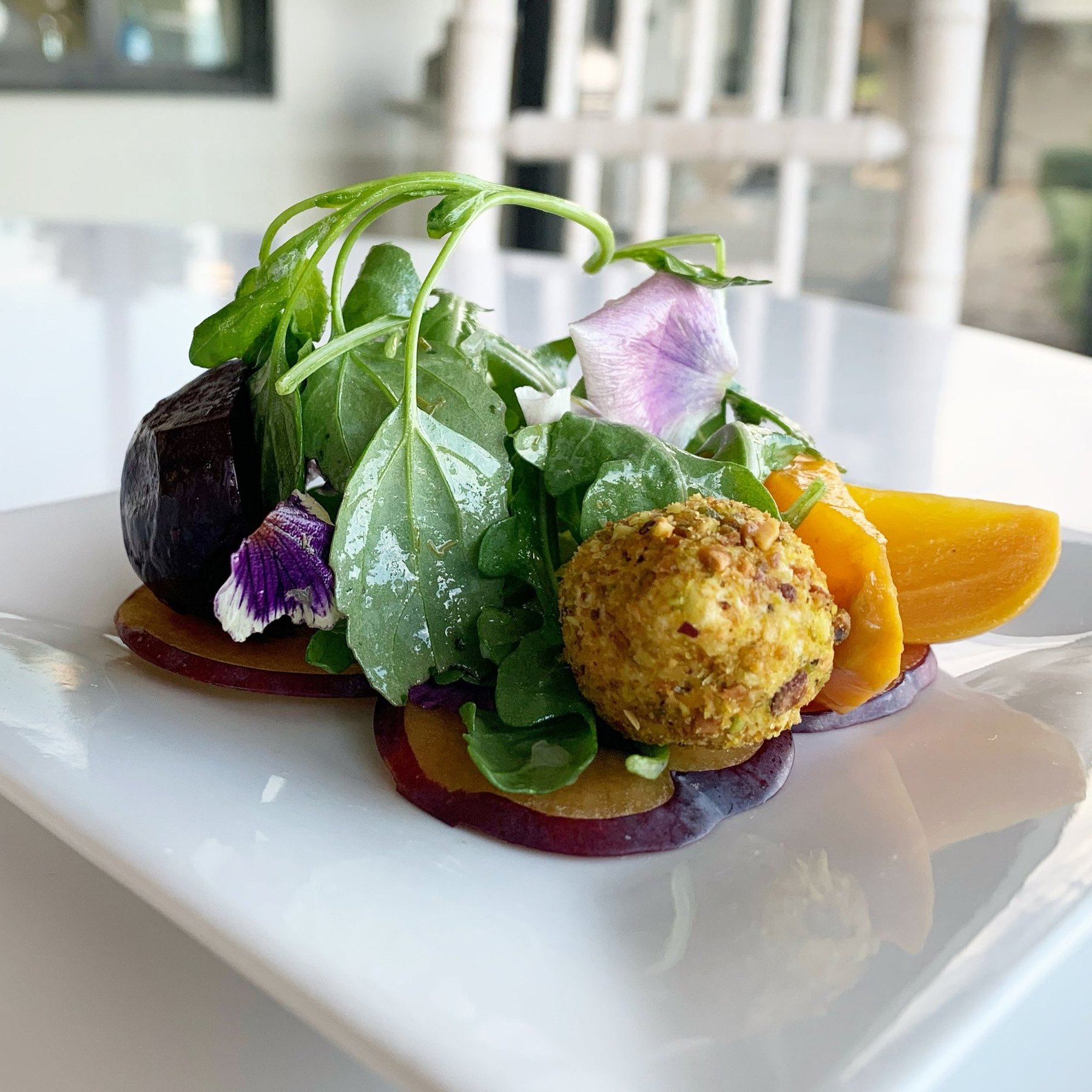 A roasted beet salad with a pistachio-crusted goat cheese round and edible flowers.