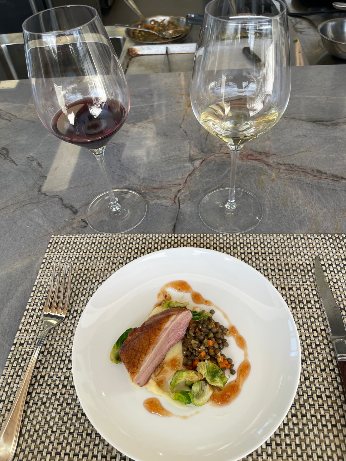 Seared duck breast with lentils and brussels sprouts, plated beside paired red and white wine.